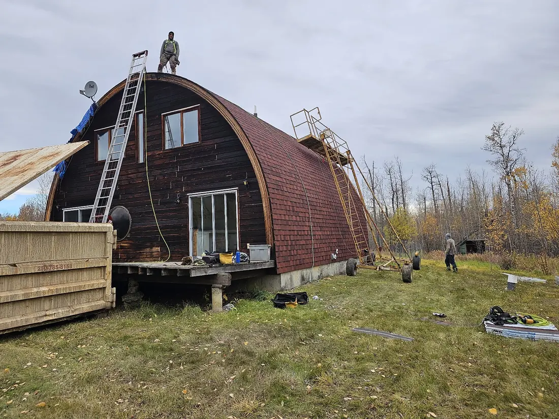 Roofer working at the crest of a full barn arch roof with ladders set against the curve