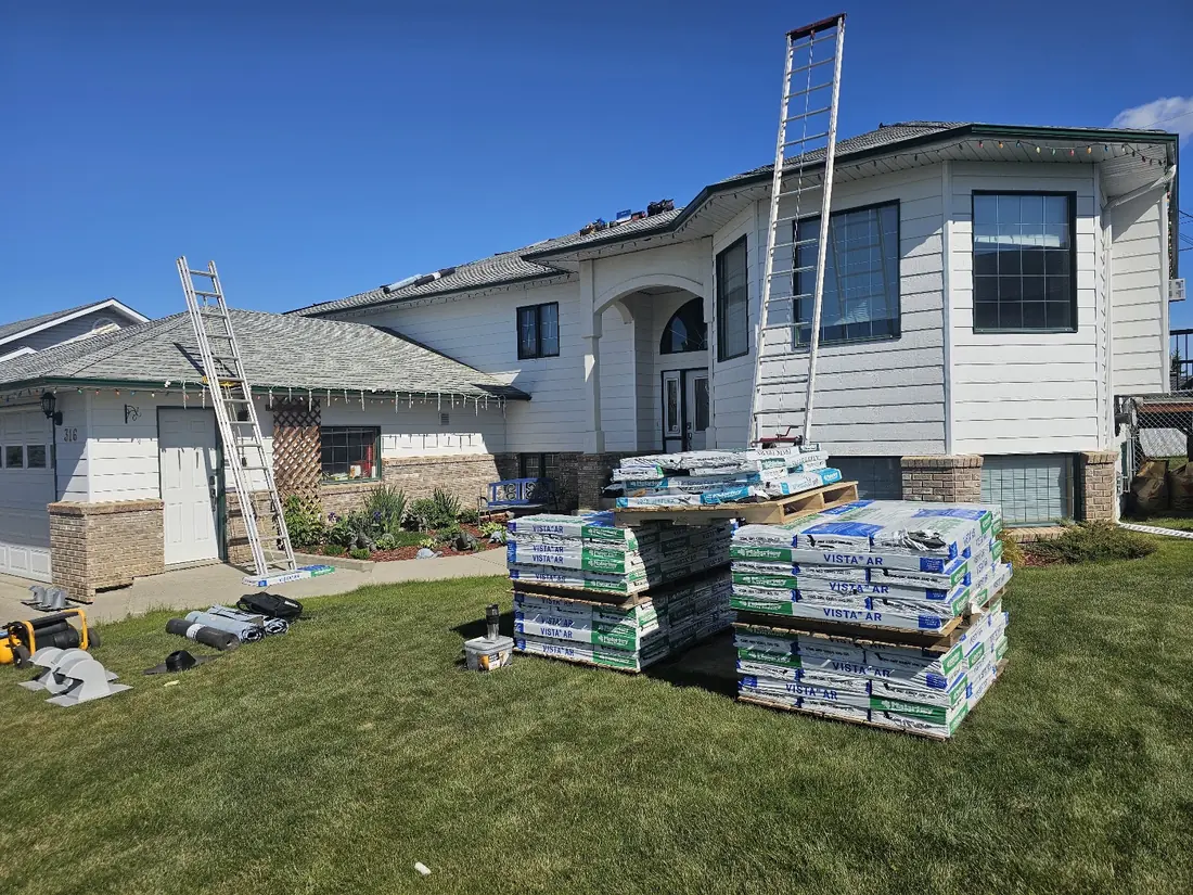 Shingle bundles staged on the lawn with ladders set up for a roof replacement