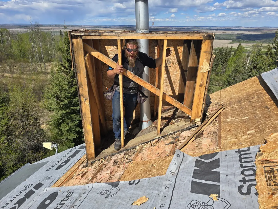 Roofer inside a reframed chimney chase during a re-roof, ice-and-water membrane run around the penetration
