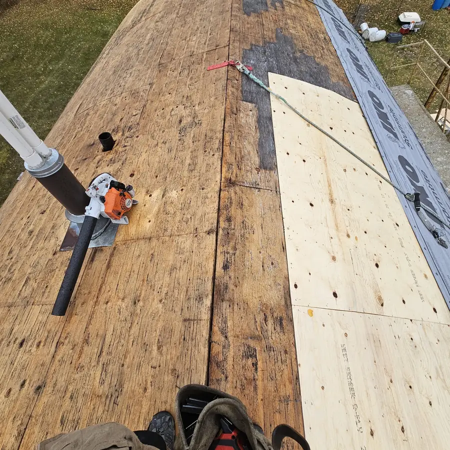 Roof deck stripped to bare wood during a Raptor tear-off, with new patch panels and a saw on the ridge