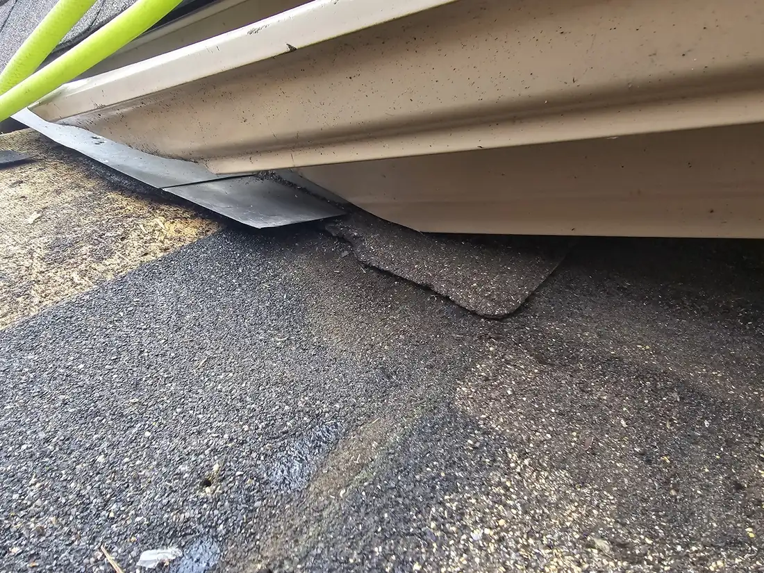 Close-up of roof layers at an eave: waterproof membrane and metal drip edge under the shingle
