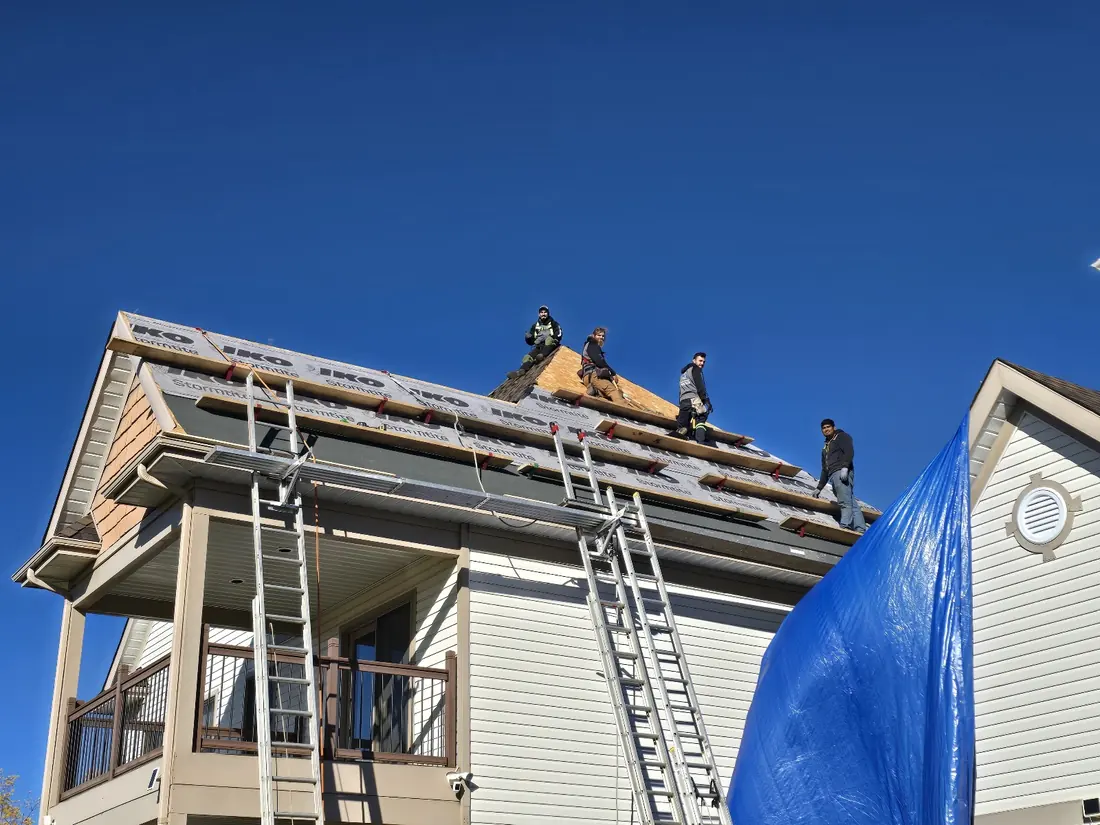 Stacked ladders reaching the top section of a three-storey house, deck protected by tarps, crew working above