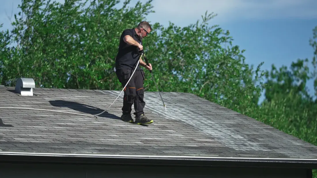 Rejuvenation crew member spraying plant-based treatment across an asphalt shingle roof in the South Peace